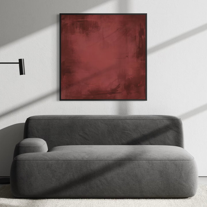 A modern gray fabric sofa in a minimalist living room setting, positioned beneath a square framed wall art piece with a textured deep red abstract design. A black floor lamp stands to the left, and soft window shadows are cast across the sofa and wall.