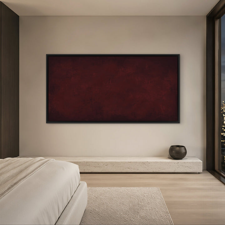 A modern bedroom interior with a large rectangular dark red wall art piece centered on a light beige wall, next to a floor-to-ceiling window showing a city skyline at dusk.
