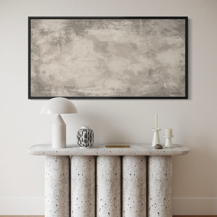 A large framed abstract canvas print with textured gray and beige brushstrokes hangs on a light beige wall above a modern console table with terrazzo-like columns. The room is styled with a white mushroom lamp, a black-and-white patterned vase, and minimalist white candle holders.