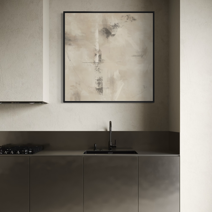 A framed abstract art print with beige, gray, and black tones hangs on a textured light beige wall above a modern kitchen counter with a sink and matte dark gray cabinets.