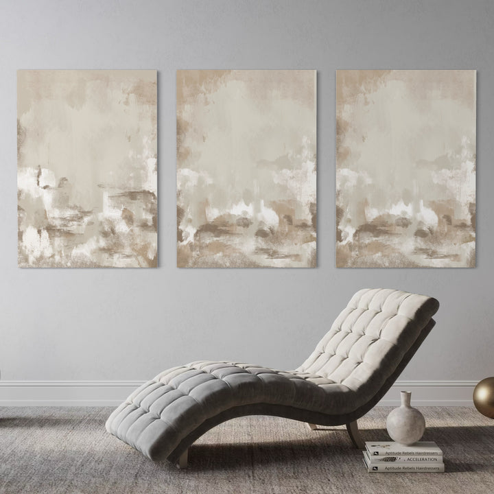 Neutral Beige Abstract Triptych Above a Tufted Grey Chaise With Books, Ceramic Vase, and Brass Orb—Serene Wall Art to Elevate a Modern Reading Corner.